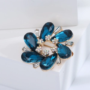 Macro detail of a dark blue crystal floral wreath brooch on a minimalist white pedestal