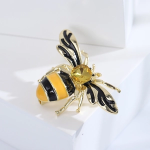 Minimalist gold alloy bee brooch with yellow gemstone and enamel details on white background