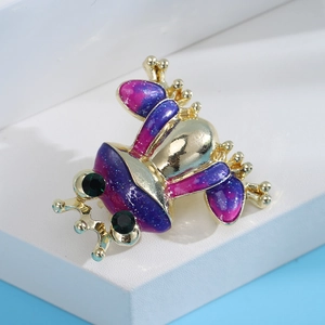 Close-up of a creative gold-plated frog brooch with purple enamel and green gem eyes