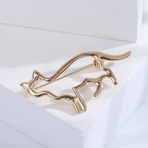 Broche chat dorée minimaliste présentée sur un bloc de pierre géométrique blanc