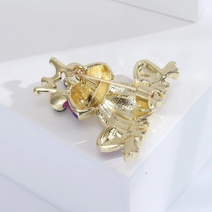 Macro detail of the polished gold finish and safety pin clasp on the frog brooch back