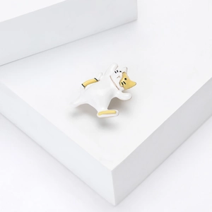 Detailed close-up of a white dancing cat enamel brooch on a minimalist white platform
