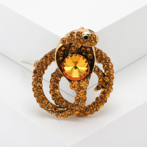 Macro shot of cobra brooch with amber rhinestones on a white geometric stand