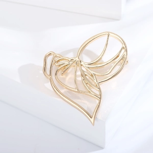 Macro shot of gold-plated abstract hollow brooch with heart and leaf motif on white prop