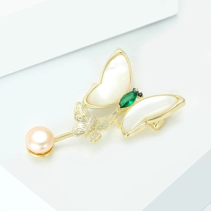 Detail of butterfly brooch with shell wings, green gem, and pink pearl on a white stand