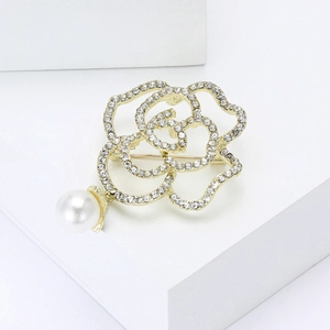 Vue détaillée de la broche camélia dorée avec strass et un pendentif perle blanche