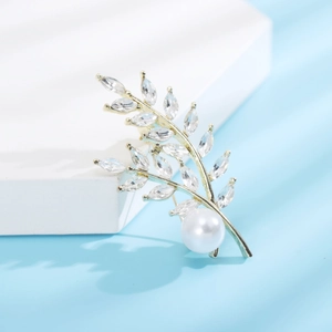 Dettaglio di un'elegante spilla a foglia dorata con cristalli e grande perla bianca