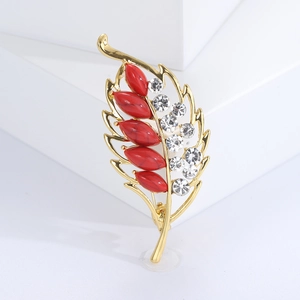 Close-up of golden leaf brooch with red stones and sparkling white rhinestones inlay