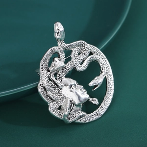 Détail macro de la broche Méduse vintage argentée avec textures de serpents sur fond vert foncé