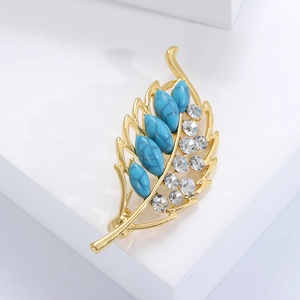 Macro detail of leaf-shaped gold brooch with blue stones and white crystals