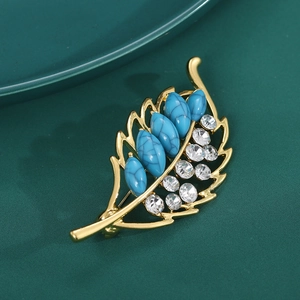 Close-up of golden leaf brooch featuring blue turquoise stones and sparkling rhinestones