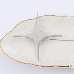 Close-up of a silver minimalist four-pointed star brooch on a gold-rimmed white plate