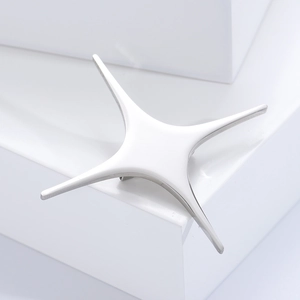 Detailed macro view of a polished silver four-pointed star brooch on minimalist props