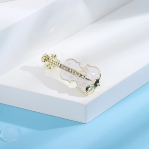 Détail de la broche violon dorée avec incrustation blanche et strass brillants sur fond bleu