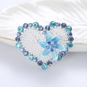 Close-up of pearl heart brooch with blue rhinestones and floral centerpiece detail