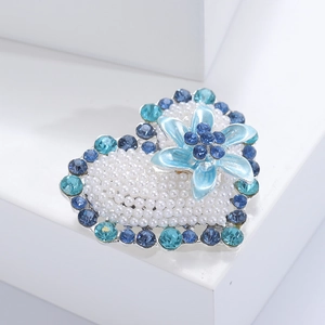 Detailed shot of a heart-shaped pearl brooch with blue rhinestones and a floral accent