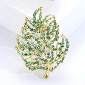 Detail of leaf brooch with green rhinestones set in gold alloy on white stand
