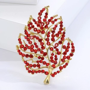 Detail of leaf-shaped gold brooch with red rhinestones on a white geometric prop