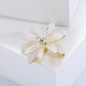 Detail of elegant gold-toned flower brooch with white petals and sparkling center crystal