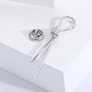 Minimalist silver metal knot brooch with hanging bars on a clean geometric platform