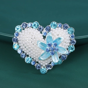 Detailed macro view of heart-shaped brooch with pearls and blue rhinestone floral accents