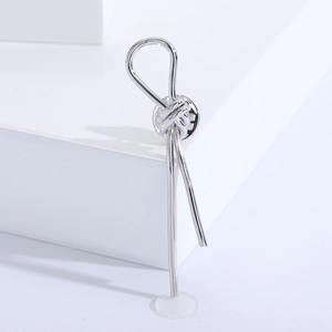Macro shot of minimalist silver knot brooch with cylindrical drops on white geometric base