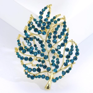 Elegant gold leaf brooch featuring brilliant blue rhinestones on a white geometric stage