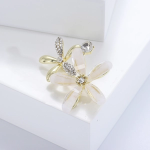 Elegante goldene Blumenbrosche mit weißen Blütenblättern und Kristallen auf weißem Podest