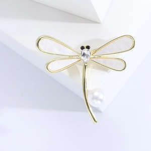 Elegante spilla a libellula dorata con ali in madreperla e perla bianca su un blocco bianco