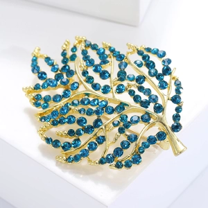 Macro shot of gold leaf brooch with navy blue rhinestones on white platform