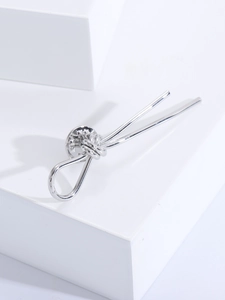 Macro view of silver knotted brooch with standard metal butterfly clasp on white block