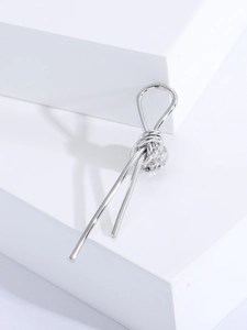 Detailed view of silver knot brooch on white geometric blocks with elegant shadows