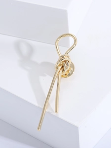 Close-up of polished gold knot brooch on white geometric stone with elegant shadows