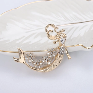 Dettaglio di una spilla a sirena dorata con pavé di strass e decorazioni floreali chic