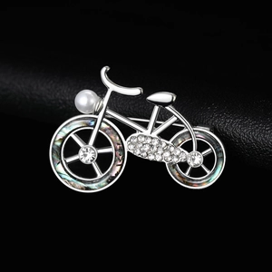 Macro detail of silver bicycle brooch with inlaid pearls, rhinestones and shell accents