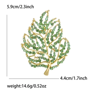 Golden leaf brooch with green rhinestones and detailed leaf veins on white background