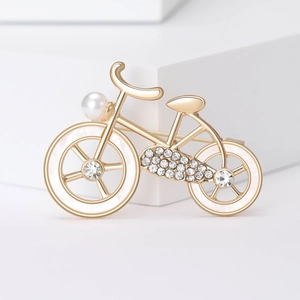 Detail of a golden bicycle brooch featuring sparkling crystals and a white pearl accent