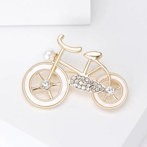 Macro view of a gold bicycle brooch featuring sparkling crystals and a white pearl accent