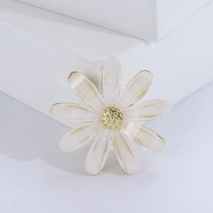 Broche marguerite minimaliste avec pétales crème et cœur doré sur un support blanc