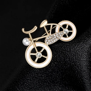 Detail of a golden bicycle brooch featuring white enamel wheels and sparkling rhinestones