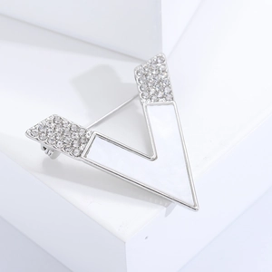 Macro shot of modern silver metal V-shaped brooch with white enamel and sparkling zircons