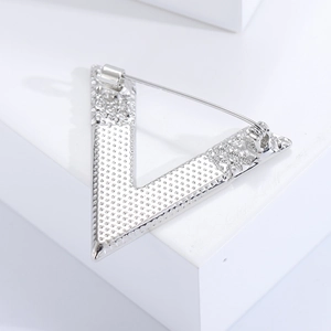 Macro detail of silver V-shaped brooch back showing pin clasp and textured metal finish