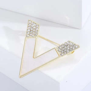 Detailed view of the gold V-shaped brooch with white enamel inlay and sparkling crystals