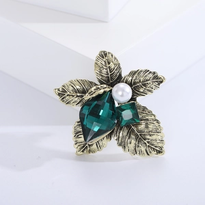 Close-up of vintage gold leaf brooch with emerald crystal and white pearl detail