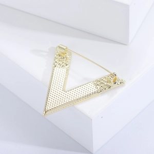 Detailed view of golden V-shaped brooch featuring textured metal and safety pin clasp