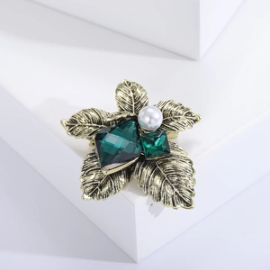 Macro shot of vintage emerald crystal flower brooch with gold metal petals and pearl detail