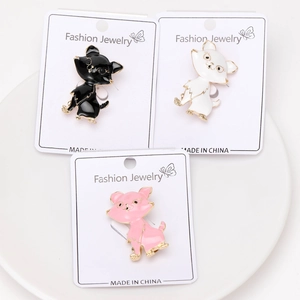 Close-up of three cute enamel cat brooches in black, white and pink on a white ceramic plate