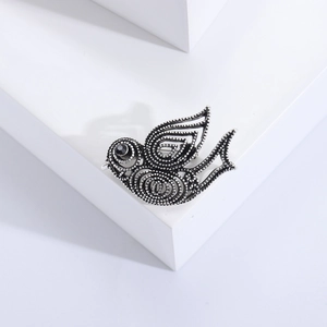 Détail d'une broche colombe vintage en métal argenté rétro avec un œil en pierre noire