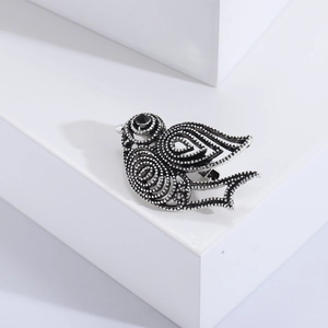 Détail macro d'une broche oiseau rétro en argent avec plumes texturées et œil serti