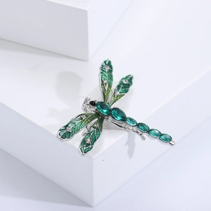 Detail of green enamel dragonfly brooch with crystals and emerald-like stones on white blocks